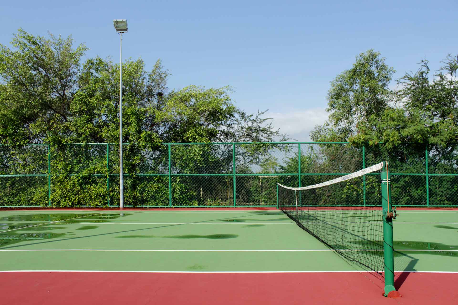 tennis-court-fencing-sports-construction-group-01 A view of a tennis court featuring a net, boundary lines. | Featured image for the Understanding the Different Types of Tennis Court Fencing blog.